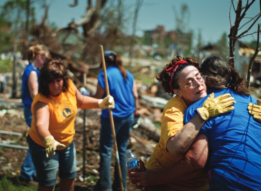 Lions volunteers comforting each other while clearing debris after a disaster